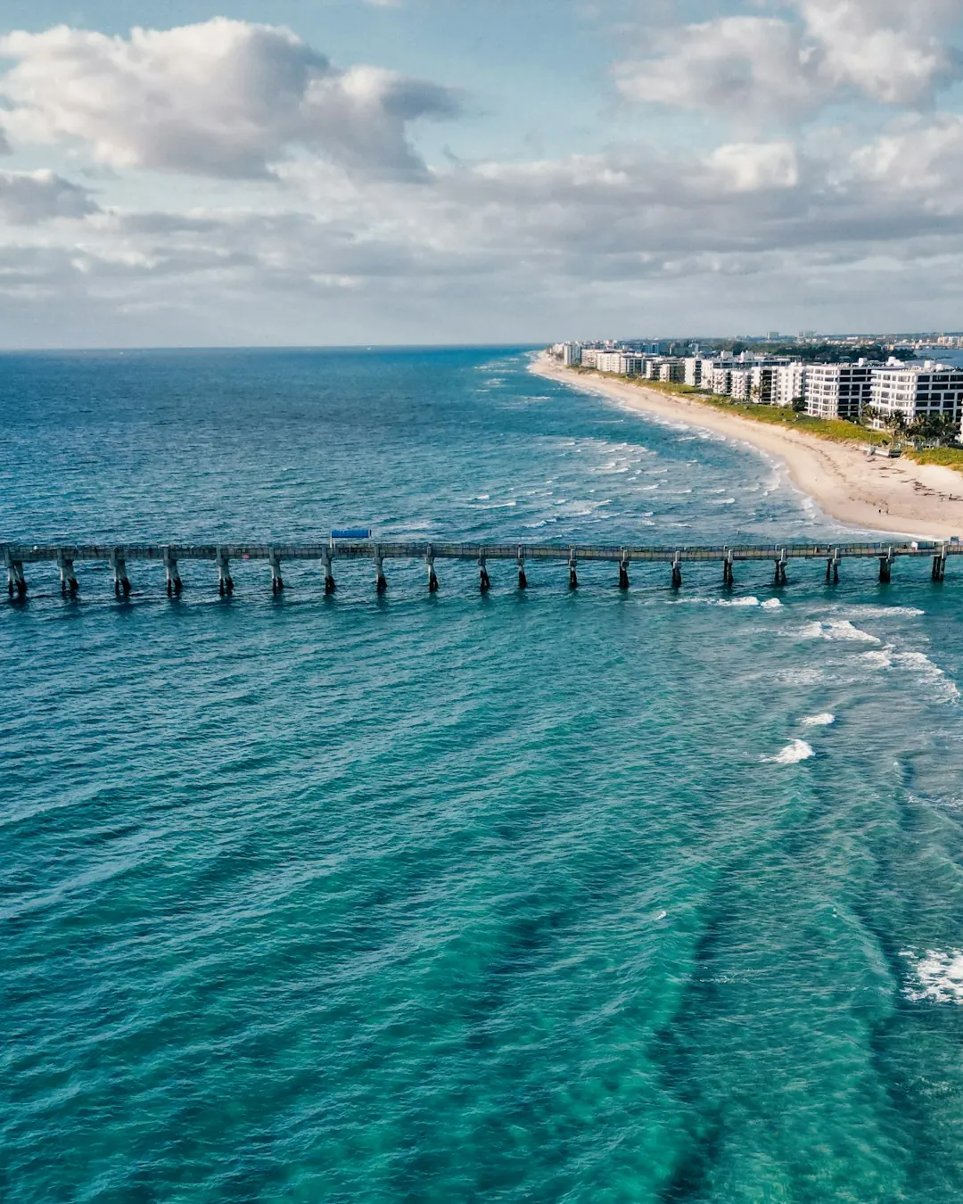 Aerial view of a pier and turquoise water along the Palm Beach shoreline